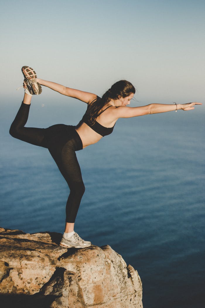 Woman practicing yoga in Dancers pose on a cliff with ocean view, Cape Town.